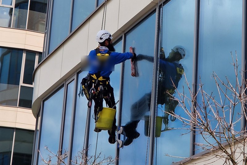 Rope-access technicians in full safety harness and helmet cleaning windows on a commercial office building